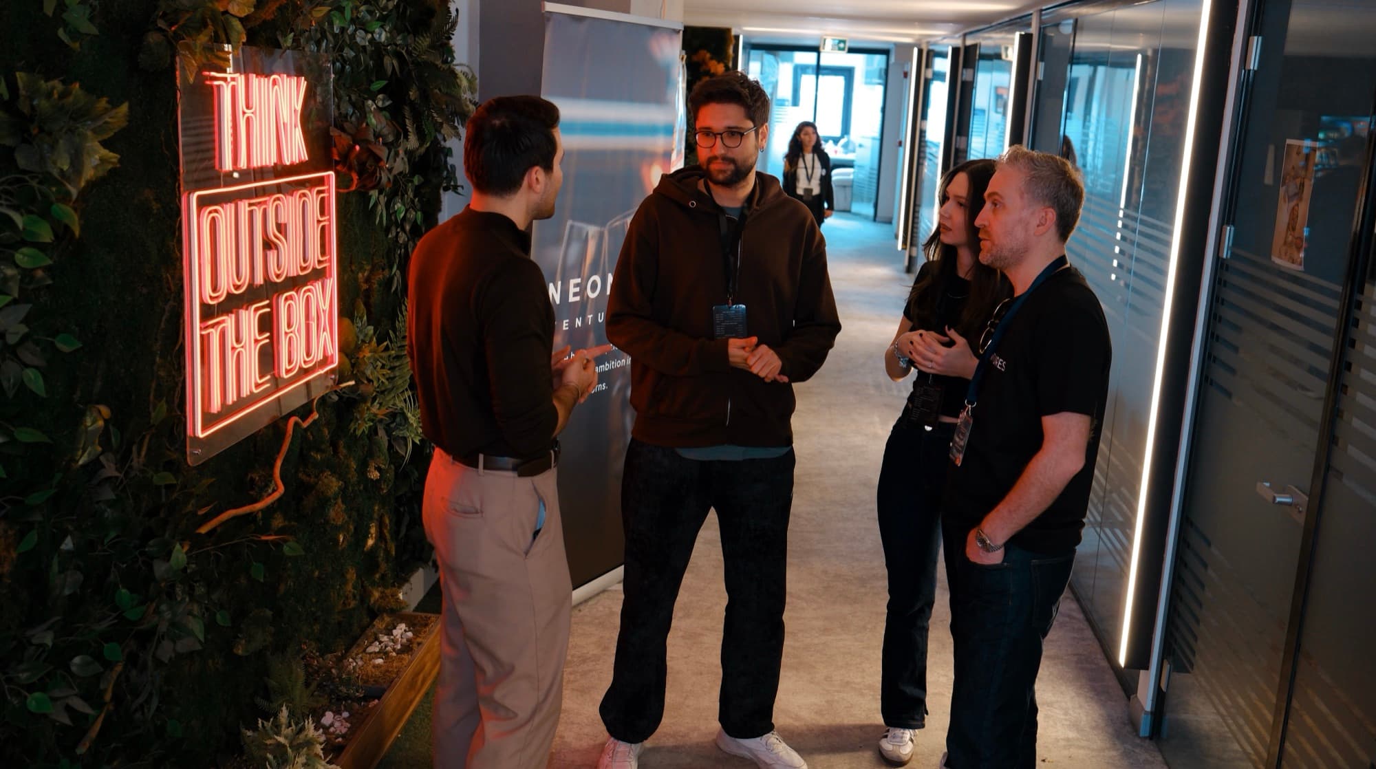 Tyler Blackford talking with the team in the Neon Apps office in Istanbul, beside the Think Outside The Box neon sign
